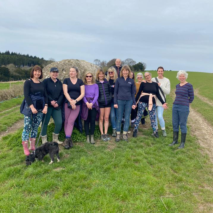 A group of students and a small dog on the Downs beside a large stone