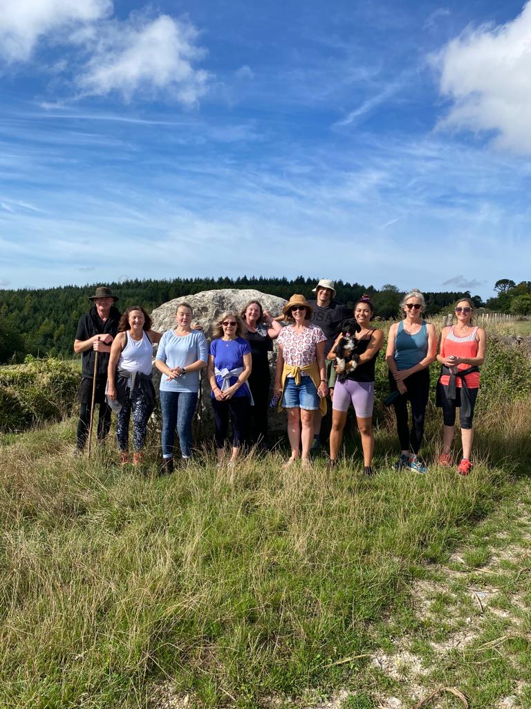 A group of students standing in front of a large stone on the Downs under a blue sky