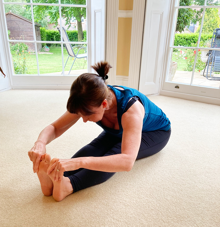 Jane in a seated forward fold on a cream carpet, garden doors open behind her