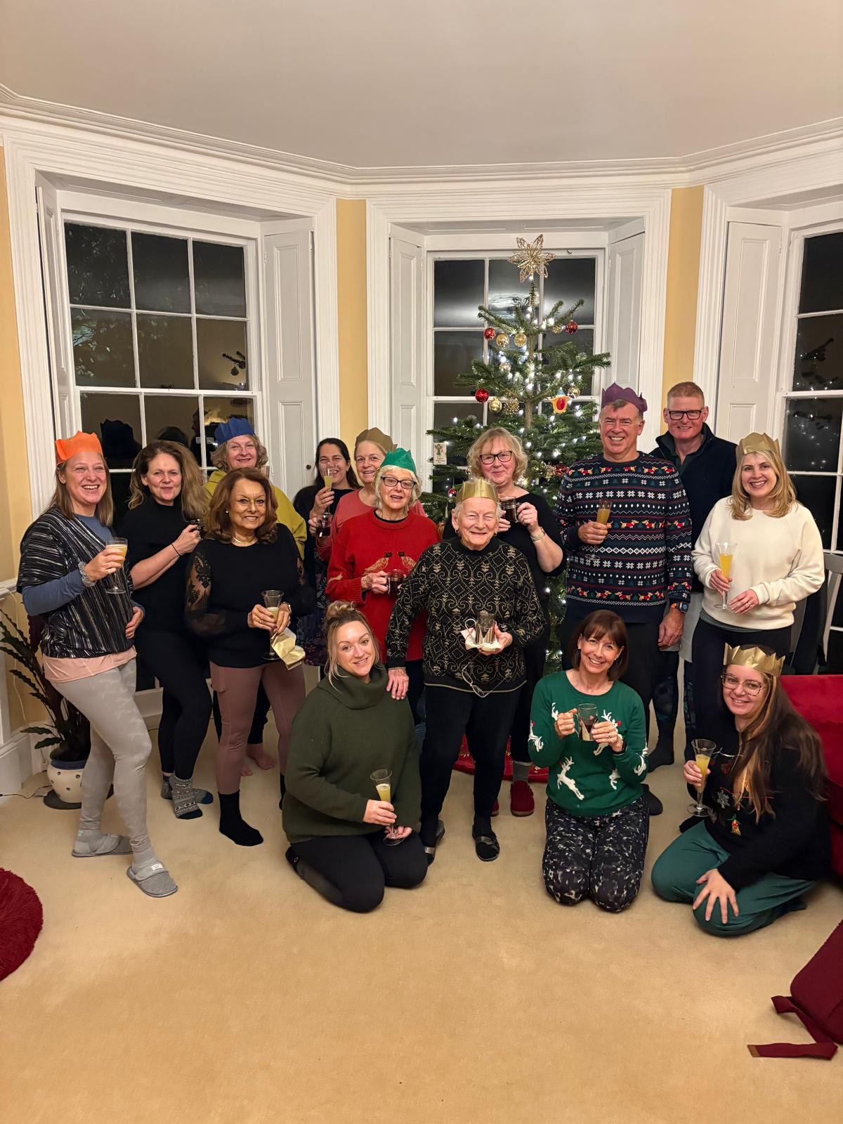 A group in paper crowns gathered round a Christmas tree in a bay-windowed room