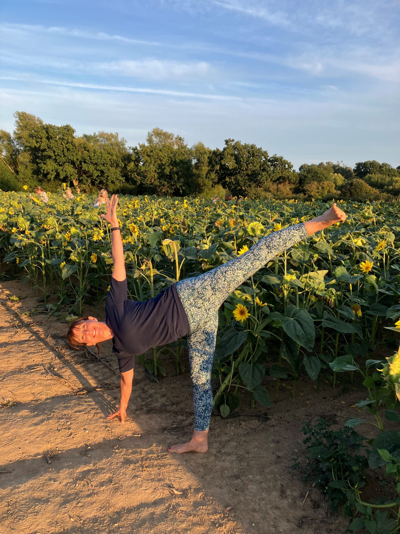 Jane in half moon pose beside a field of sunflowers in evening light